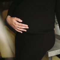 a pregnant woman standing on a stool with her hands on her stomach