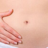 女性が両手でお腹を優しく包んでいる様子 タイトル: 産後の下っ腹ぽっこり解消法