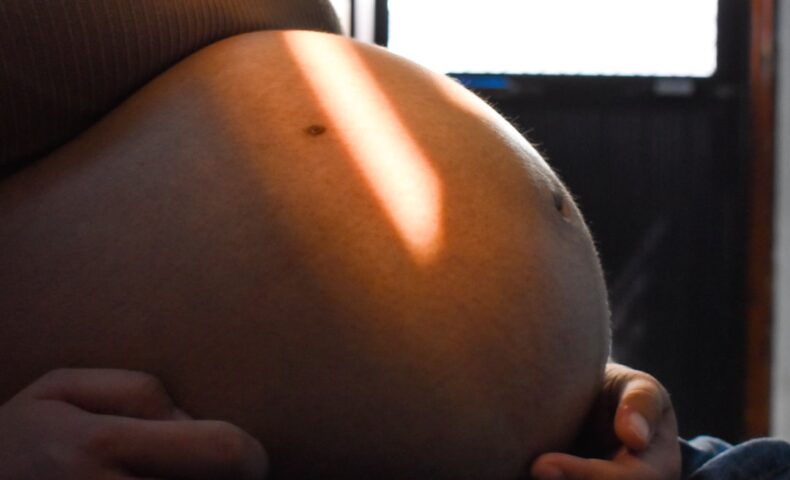 Pregnant woman's belly illuminated by sunlight.