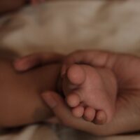 母親の手が赤ちゃんの小さな足を優しく包んでいる様子