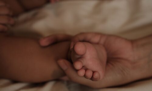 母親の手が赤ちゃんの小さな足を優しく包んでいる様子