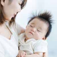 白い服を着た母親が赤ちゃんを抱いて優しく見つめている様子 タイトル: 産後ダイエットいつまでが勝負？母子の写真