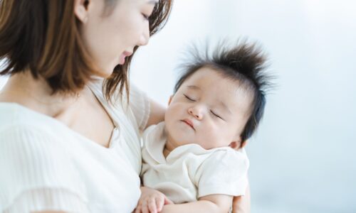 白い服を着た母親が赤ちゃんを抱いて優しく見つめている様子 タイトル: 産後ダイエットいつまでが勝負？母子の写真