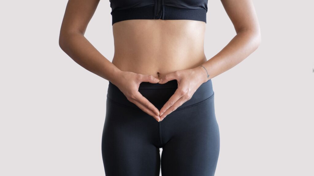 黒いスポーツウェアを着た女性がお腹の前でハートの形を作っている様子