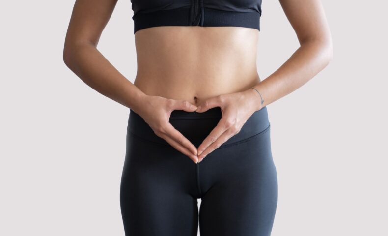 黒いスポーツウェアを着た女性がお腹の前でハートの形を作っている様子